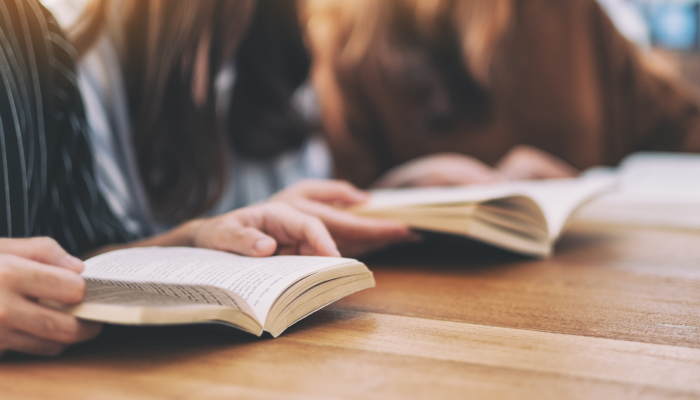 3 people sitting at the table reading a book.