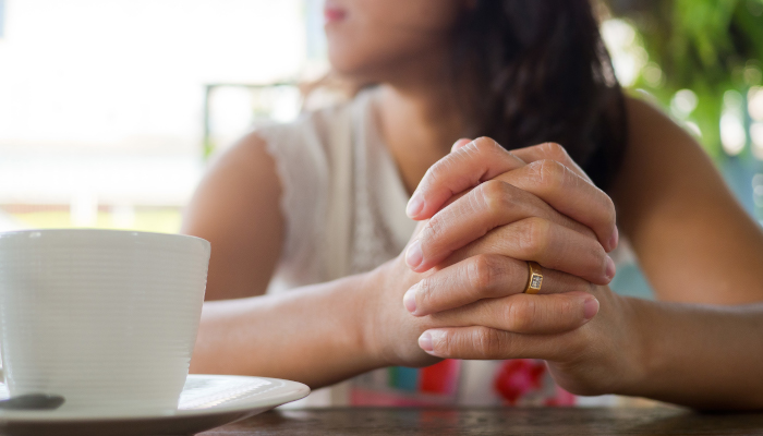 Women sitting at table praying with a cup of tea on the table