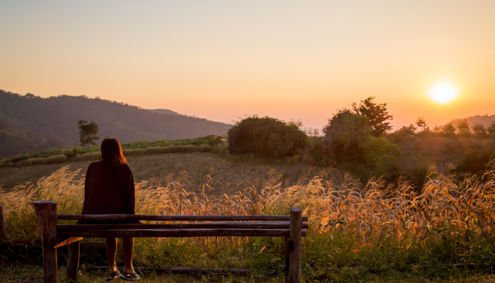 Woman sitting on bench looking at sunset
